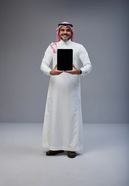 رجل سعودي بالزي التقليدي يحمل جهاز لوحي شاشة فارغة