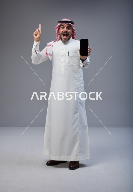 رجل سعودي يحمل هاتف ذكي بشاشة فارغة في الاستوديو