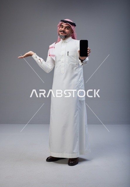 رجل سعودي بالزي التقليدي يحمل هاتف ذكي