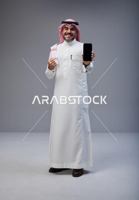 رجل سعودي بالزي التقليدي يحمل هاتف ذكي بشاشة فارغة