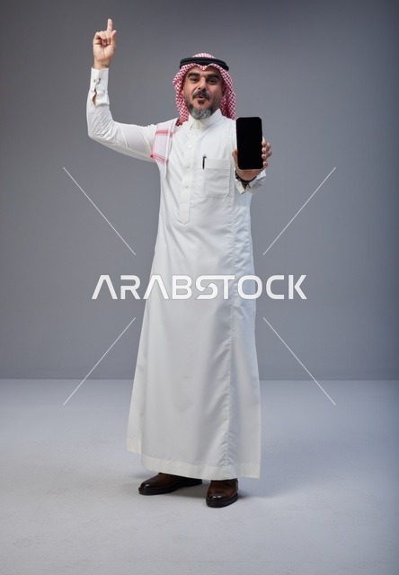 رجل سعودي بالزي التقليدي يحمل هاتف ذكي بشاشة فارغة