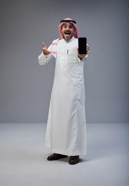 رجل سعودي بالزي التقليدي يحمل هاتف ذكي في استوديو