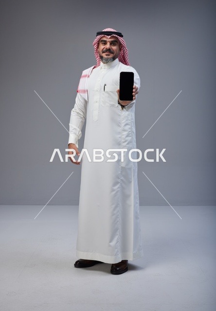 رجل سعودي بالزي التقليدي يحمل شاشة هاتف ذكي