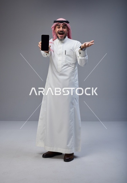 رجل سعودي يحمل هاتف ذكي بتعبير وجه مندهش
