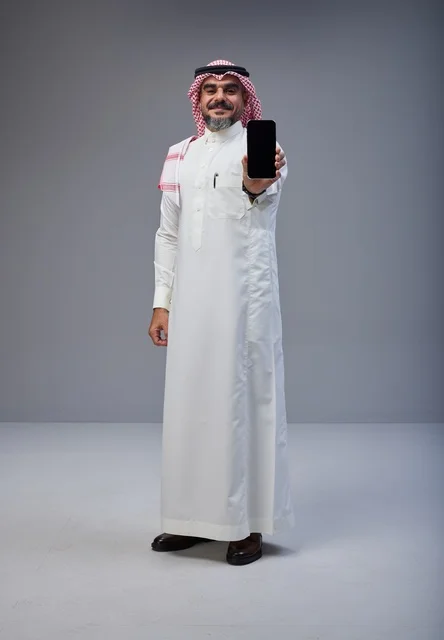 رجل سعودي بالزي التقليدي يحمل هاتف ذكي بشاشة فارغة