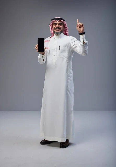 رجل سعودي بالزي التقليدي يمسك هاتف ذكي في استوديو