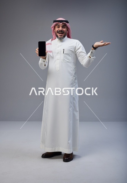 رجل سعودي بالزي التقليدي يمسك هاتف ذكي بشاشة فارغة