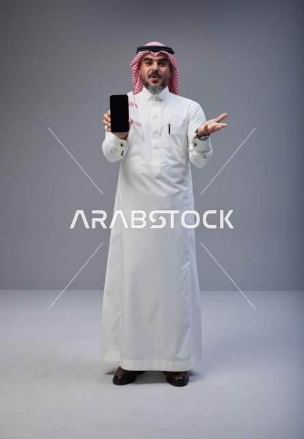رجل سعودي بالزي التقليدي يحمل هاتف ذكي في الاستوديو