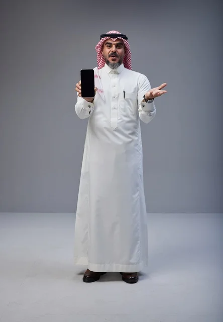 رجل سعودي بالزي التقليدي يحمل هاتف ذكي في الاستوديو