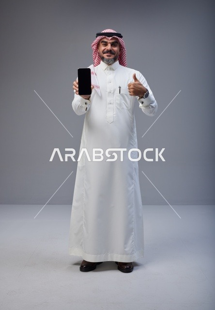 رجل سعودي يحمل هاتفاً ذكياً مع علامة الإعجاب