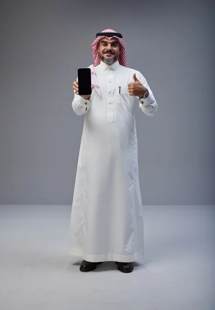 رجل سعودي يحمل هاتفاً ذكياً مع علامة الإعجاب