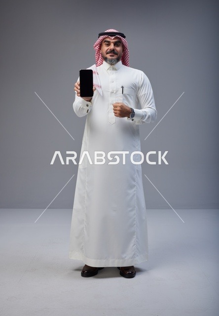 رجل سعودي بالزي التقليدي يحمل هاتف ذكي