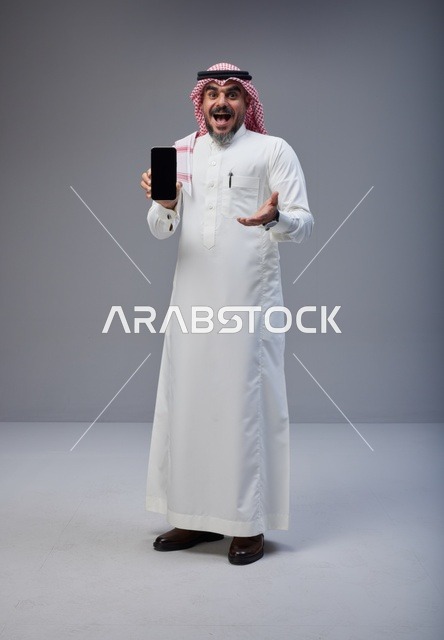 رجل سعودي بالزي التقليدي يحمل هاتف ذكي