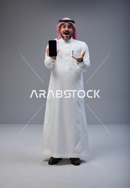 رجل سعودي بزي تقليدي يحمل هاتف ذكي في استوديو