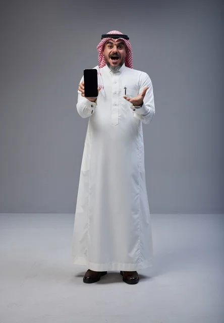 رجل سعودي بزي تقليدي يحمل هاتف ذكي في استوديو