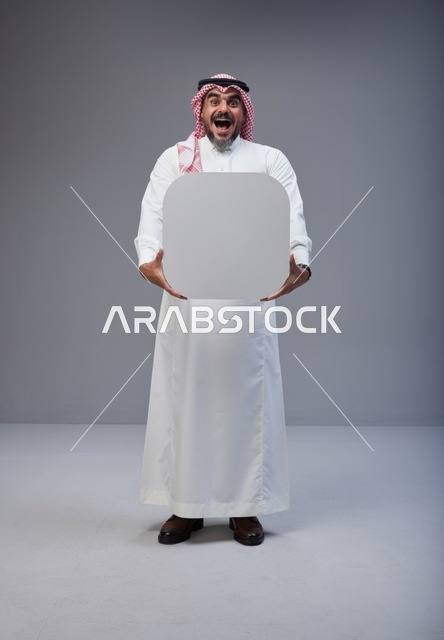 رجل سعودي مندهش يحمل لوحة بيضاء فارغة في الاستوديو