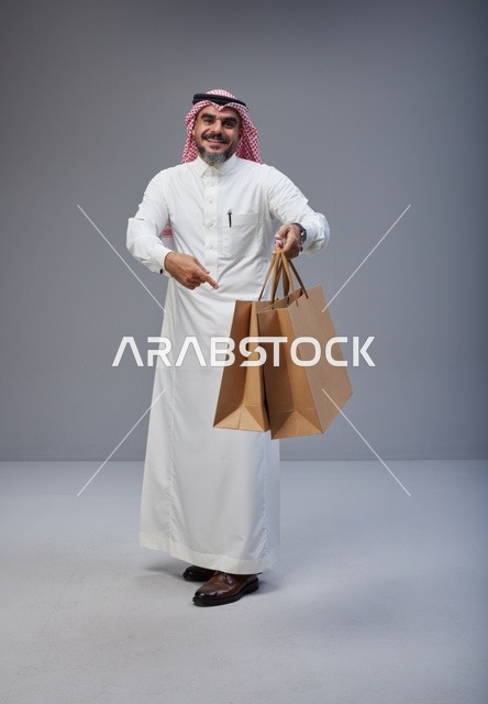 رجل سعودي بزي تقليدي يحمل أكياس تسوق ورقية في الاستوديو