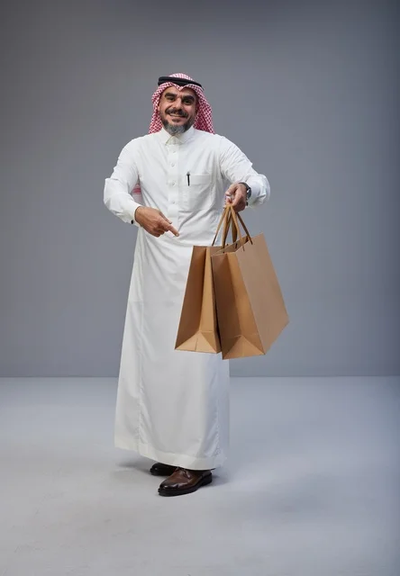 رجل سعودي بزي تقليدي يحمل أكياس تسوق ورقية في الاستوديو