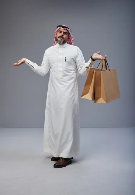 رجل سعودي يحمل أكياس تسوق بتعبير حائر في الاستوديو