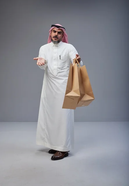 رجل سعودي يحمل أكياس تسوق ورقية في الاستوديو رجل سعودي يحمل أكياس تسوق ورقية في الاستوديو