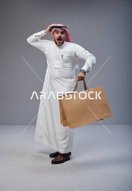 رجل سعودي مندهش يحمل أكياس تسوق في الاستوديو