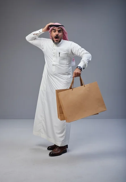 رجل سعودي مندهش يحمل أكياس تسوق في الاستوديو رجل سعودي مندهش يحمل أكياس تسوق في الاستوديو