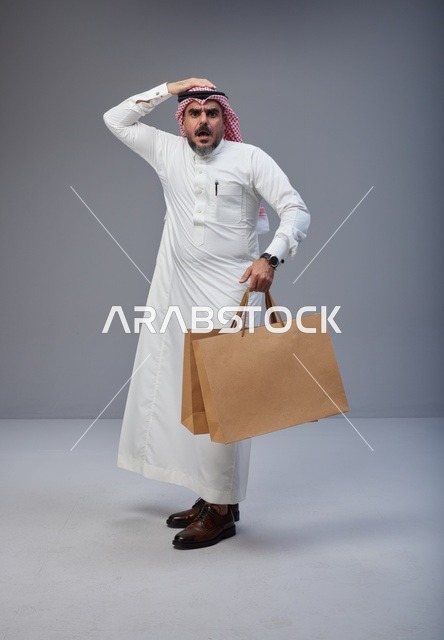 رجل سعودي مصدوم يحمل أكياس تسوق في الاستوديو