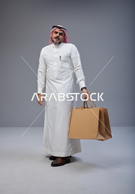 رجل سعودي بالزي التقليدي يحمل أكياس تسوق ورقية