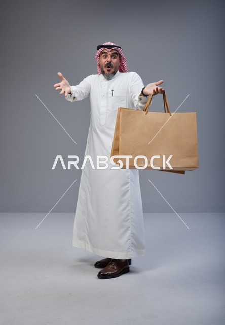 رجل سعودي يحمل أكياس تسوق بتعبيرات وجه مندهشة