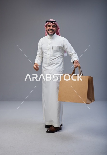 رجل سعودي بالزي التقليدي يحمل أكياس تسوق ورقية