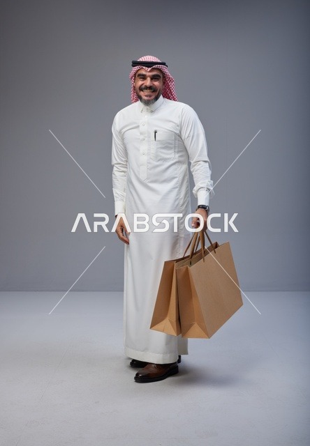 رجل سعودي بالزي التقليدي يحمل أكياس تسوق في استوديو