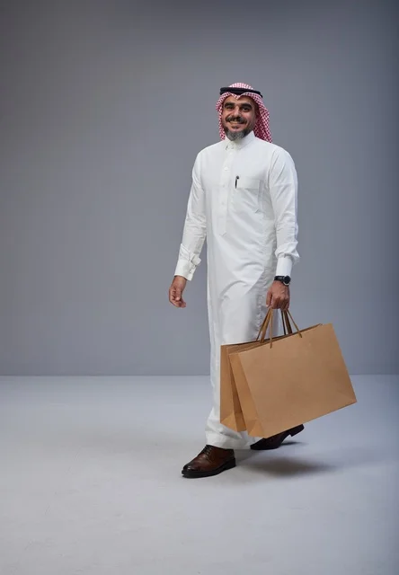 Saudi man in traditional attire holding shopping bags