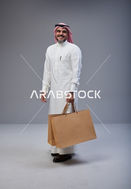 رجل سعودي بالزي التقليدي يحمل أكياس تسوق