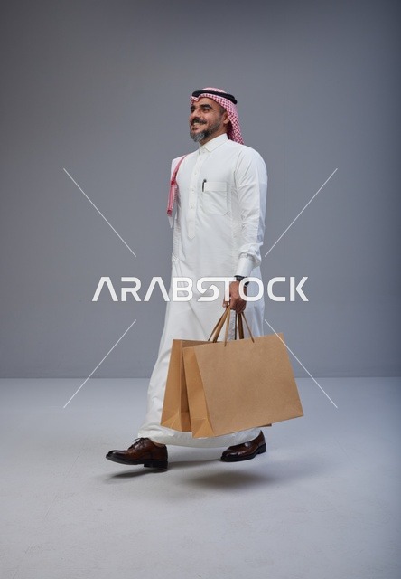 رجل سعودي بالزي التقليدي يحمل أكياس تسوق في استوديو