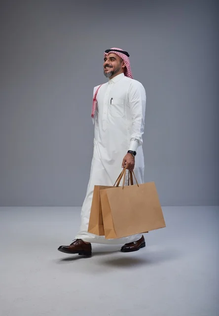 رجل سعودي بالزي التقليدي يحمل أكياس تسوق في استوديو
