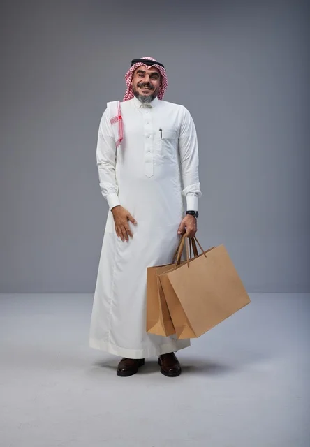 رجل سعودي بالزي التقليدي يحمل أكياس تسوق ورقية