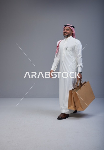رجل سعودي بالزي التقليدي يحمل أكياس تسوق