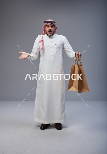رجل سعودي مندهش يحمل أكياس تسوق في الاستوديو