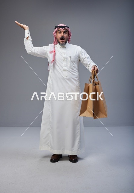 رجل سعودي مصدوم يحمل أكياس تسوق في الاستوديو