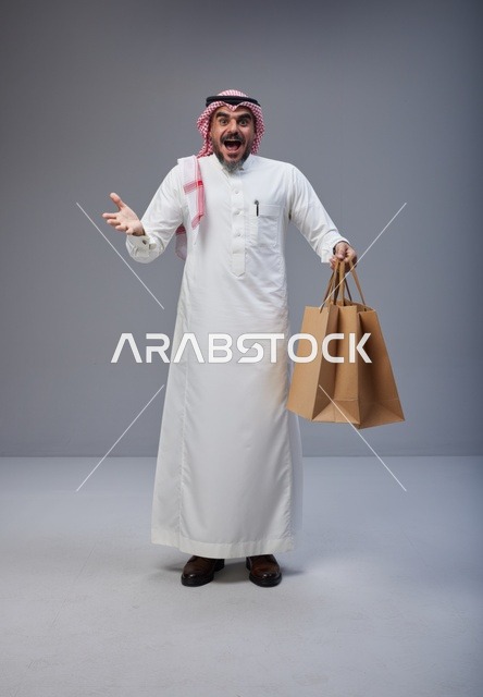 رجل سعودي متحمس يحمل أكياس تسوق في الاستوديو