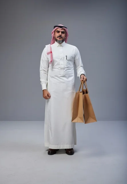رجل سعودي بالزي التقليدي يحمل أكياس تسوق ورقية