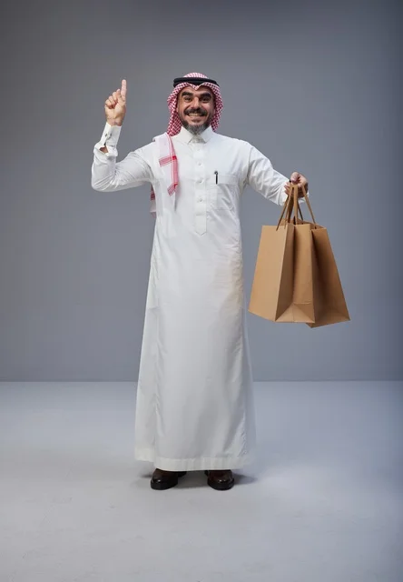رجل سعودي يحمل أكياس تسوق ويشير للأعلى في استوديو
