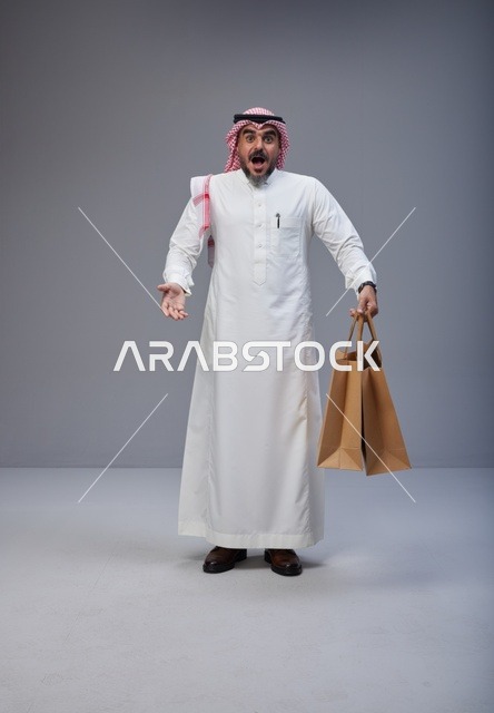 رجل سعودي مندهش يحمل أكياس تسوق في الاستوديو