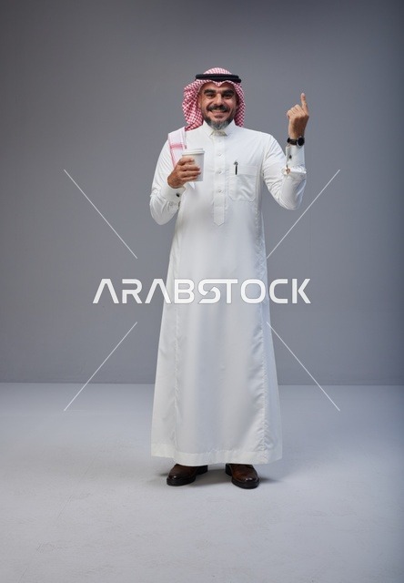 رجل سعودي بالثوب يحمل كوب قهوة ويشير للأعلى
