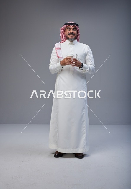 رجل سعودي بالزي التقليدي يحمل كوب ماء في الاستوديو