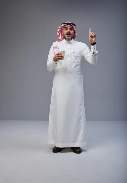 رجل سعودي يحمل كوب قهوة ويشير للأعلى في استوديو