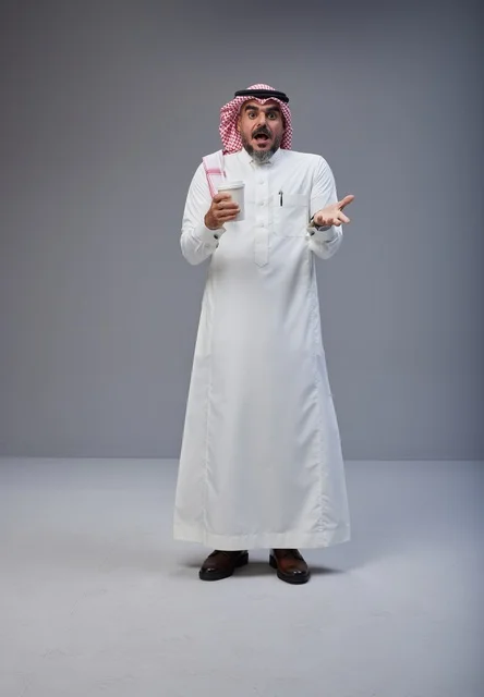 رجل سعودي مندهش يحمل كوب قهوة في استوديو رمادي