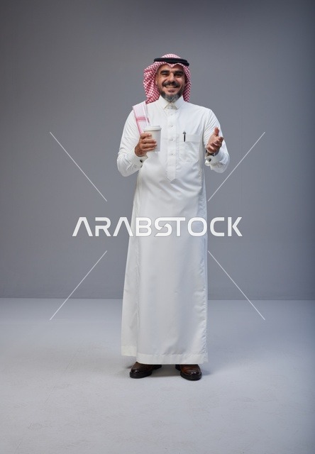 رجل سعودي بالزي التقليدي يحمل كوب قهوة في الاستوديو