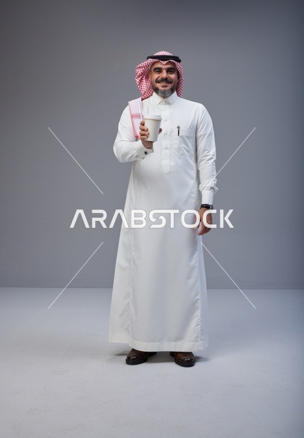 رجل سعودي بالزي التقليدي يحمل كوب قهوة في الاستوديو