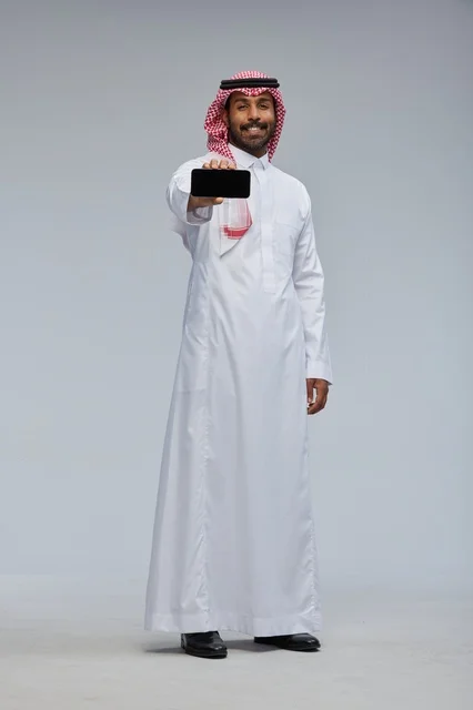رجل سعودي يمسك هاتف ذكي بالزي التقليدي